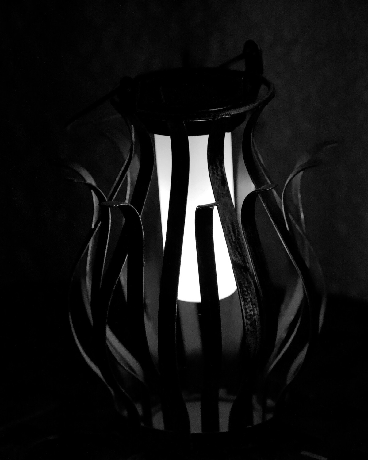 A candle glowing inside a sculpted metal lantern in a dark room